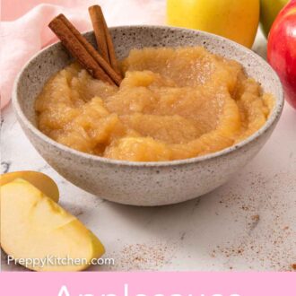 Pinterest graphic of a bowl of applesauce with two cinnamon sticks stuck inside and some apples around it.