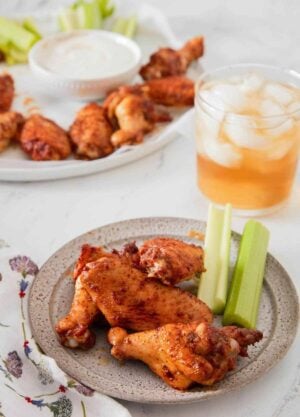A plate with three chicken wings and celery with more in the background along with an iced drink.