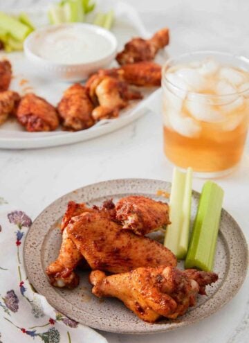 A plate with three chicken wings and celery with more in the background along with an iced drink.