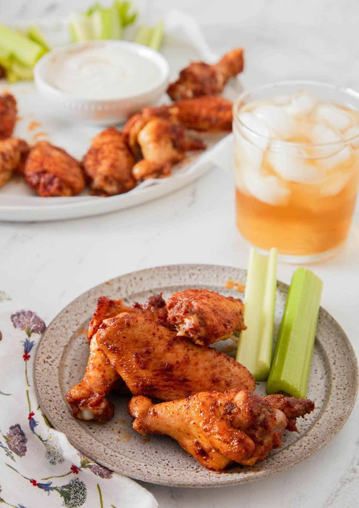 A plate with three chicken wings and celery with more in the background along with an iced drink.