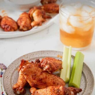 Pinterest graphic of a plate with three chicken wings and two celery sticks with more in the background along with a drink.