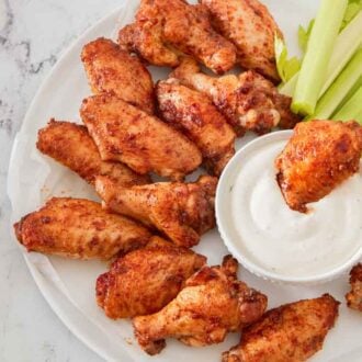 Overhead view of a platter of chicken wings with celery and a bowl with dip with one wing dipped in.