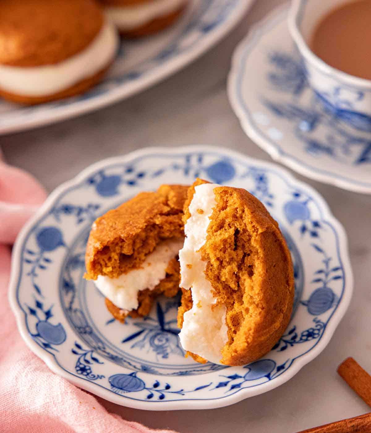 A plate with a pumpkin whoopie pie torn in half, showing the cream in the middle.