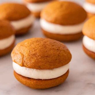 Multiple pumpkin whoopie pies on a marble surface.