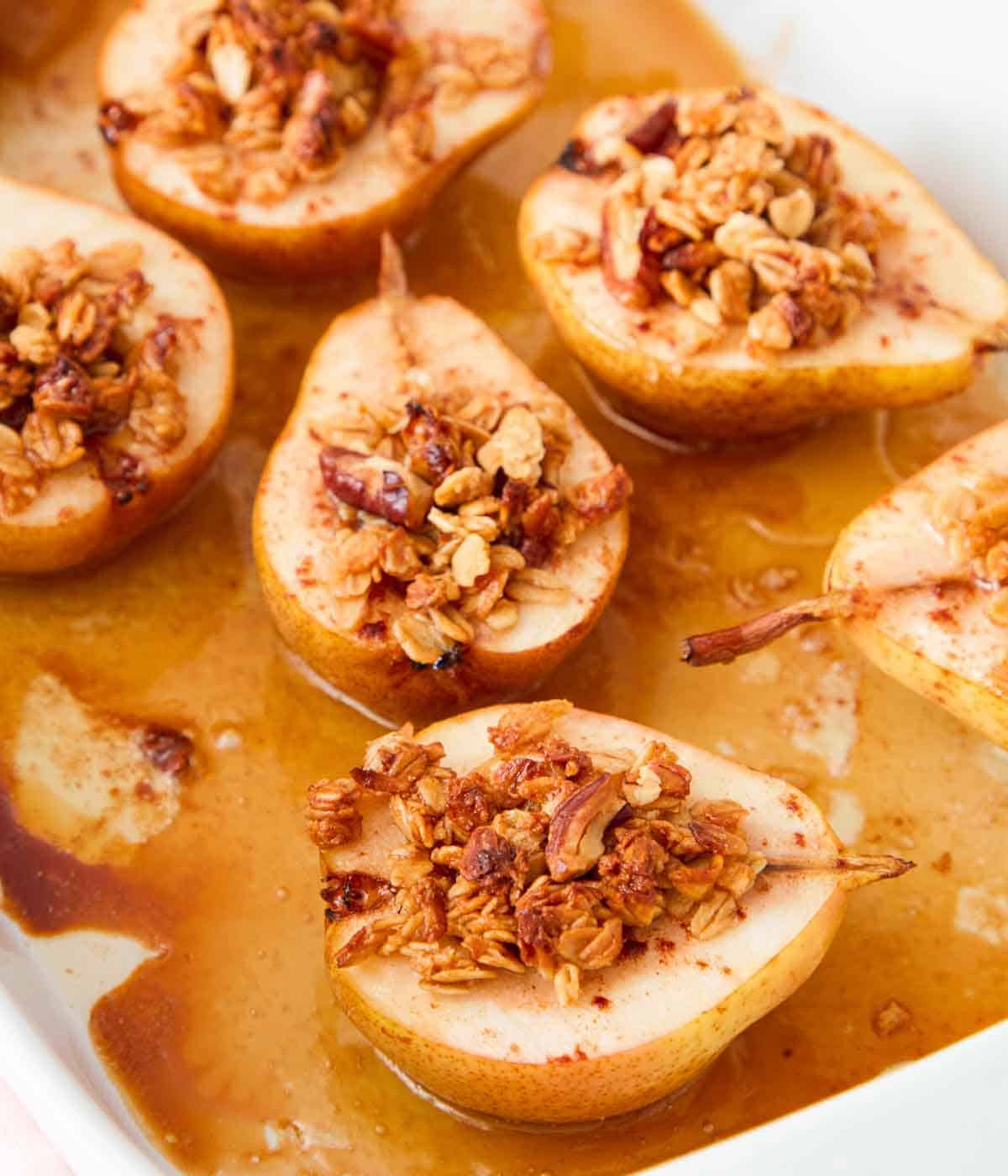 A white baking dish with baked pears with granola on top.