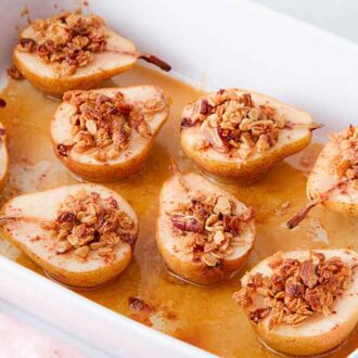 A white baking dish of multiple baked pears with granola on top.