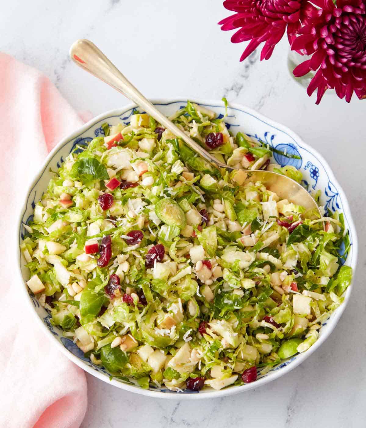 A large bowl of Brussels sprout salad with a serving spoon tucked in.