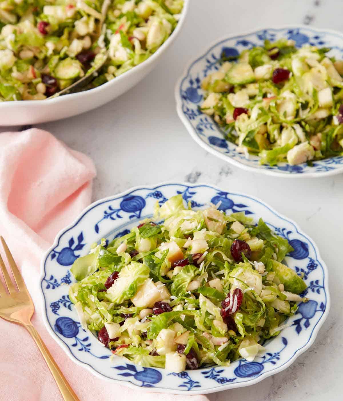 Two plates of Brussels sprout salad with a serving bowl in the background.