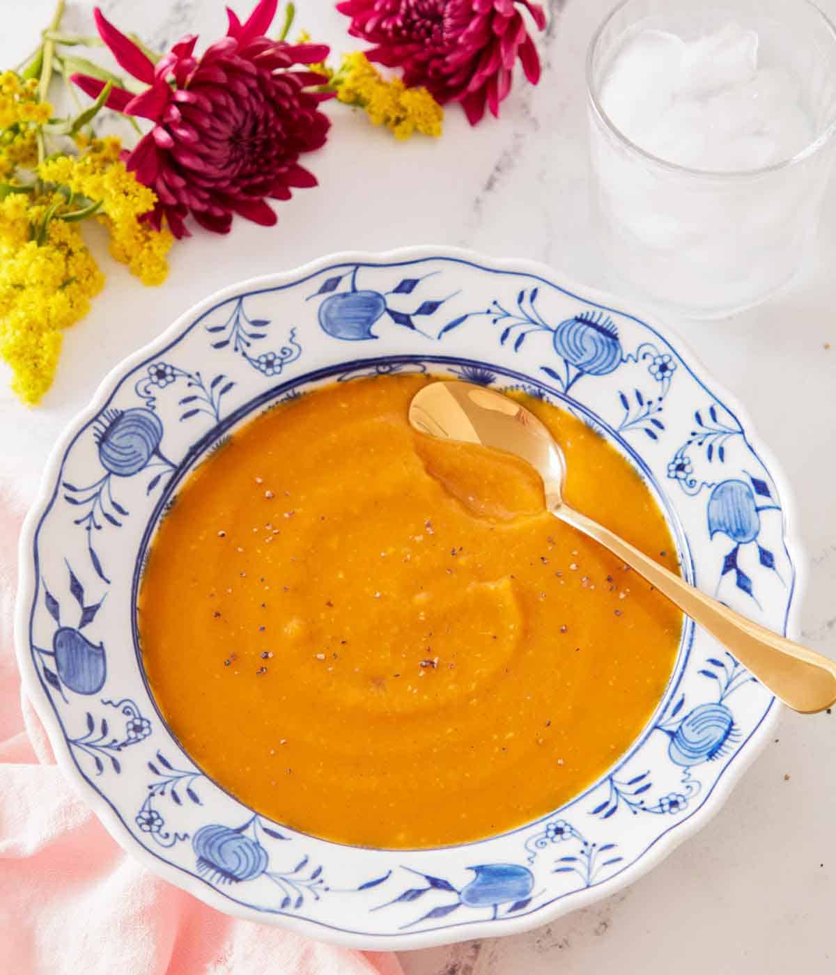 A bowl of butternut squash soup with a spoon tucked in with a glass of water off to the side.