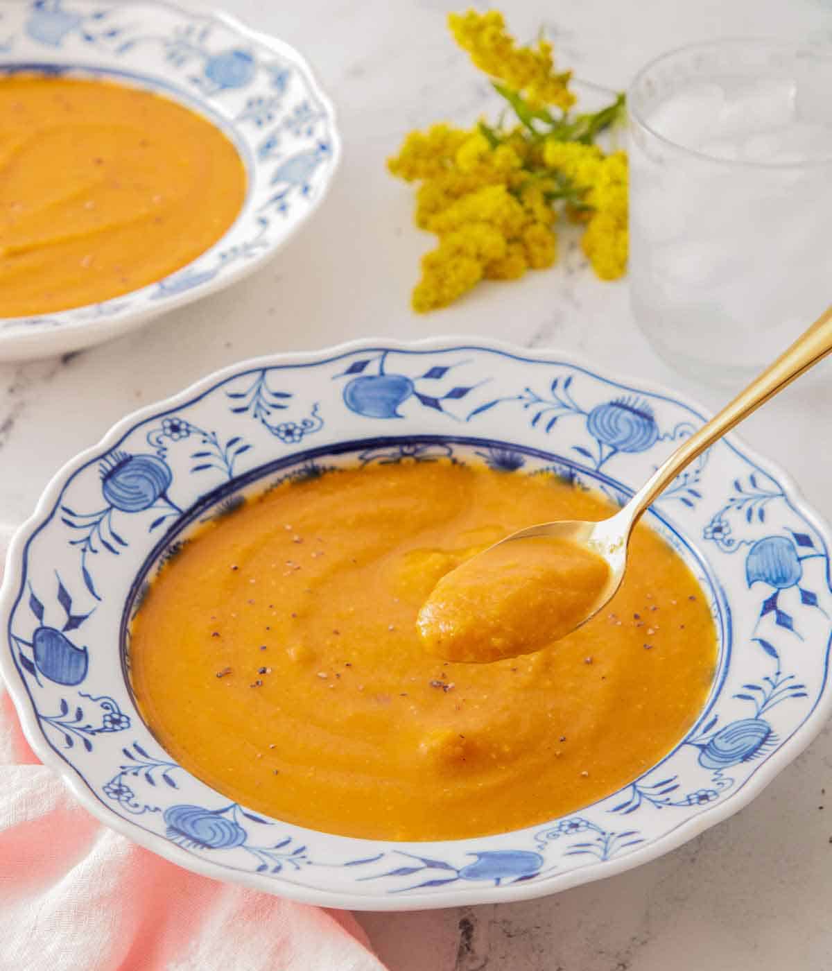 A bowl of butternut squash soup with a spoonful lifted up from the bowl.