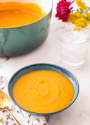 A bowl of butternut squash soup with a glass of water and pot of soup off to the side.