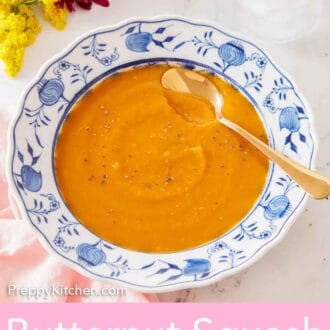 Pinterest graphic of a bowl of butternut squash soup with a spoon placed on top with some flowers off to the side.