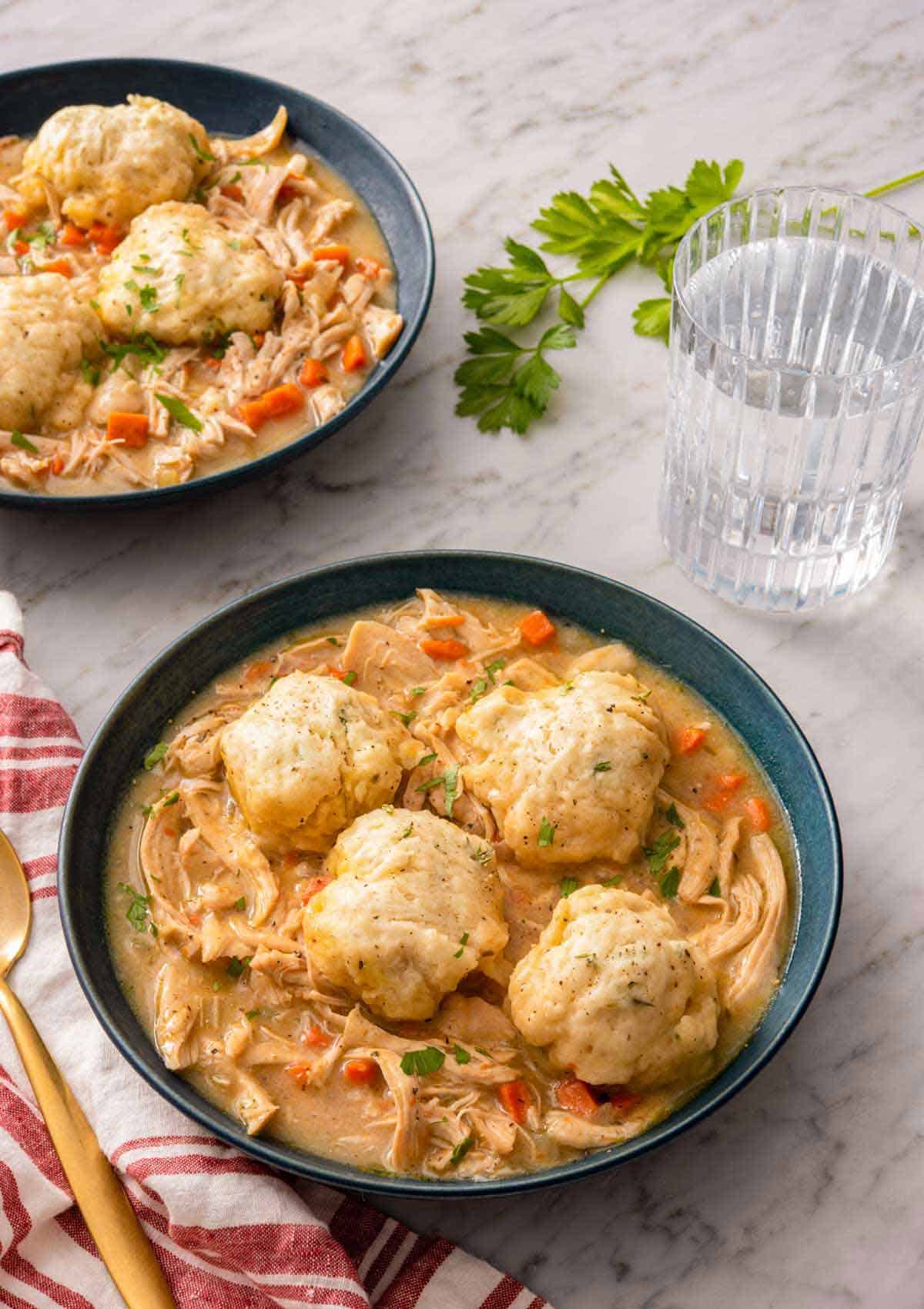 Two bowls of chicken and dumplings with one in front, with a glass of water on the side.