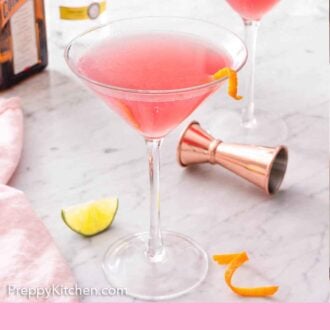 Pinterest graphic of two glasses of Cosmopolitan cocktails with the alcohol bottles in the background and garnish in the front.