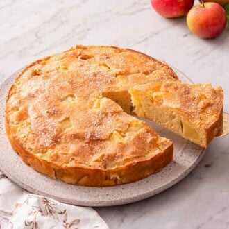 A French apple cake with a slice cut and lifted from the cake with a cake spatula.