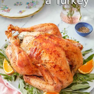 Pinterest graphic of a roasted turkey over a platter of fresh herbs and cut oranges. Flowers, plates, and pepper in the background.