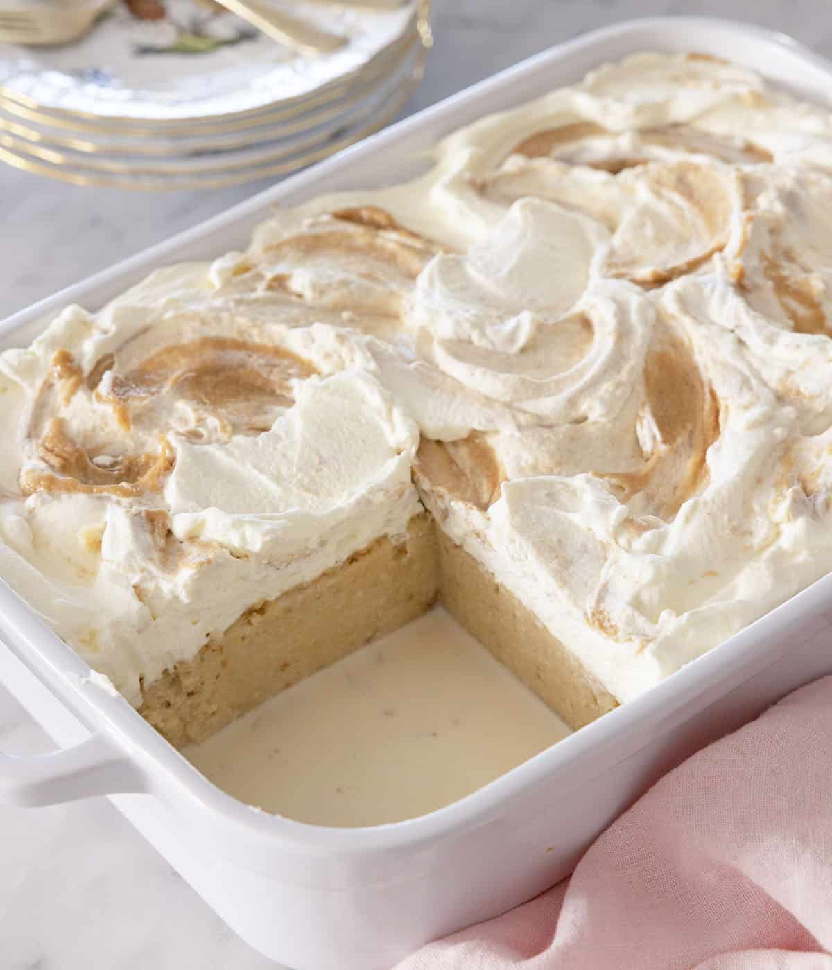 A peanut butter tres leches cake in a white baking dish with a piece removed. 