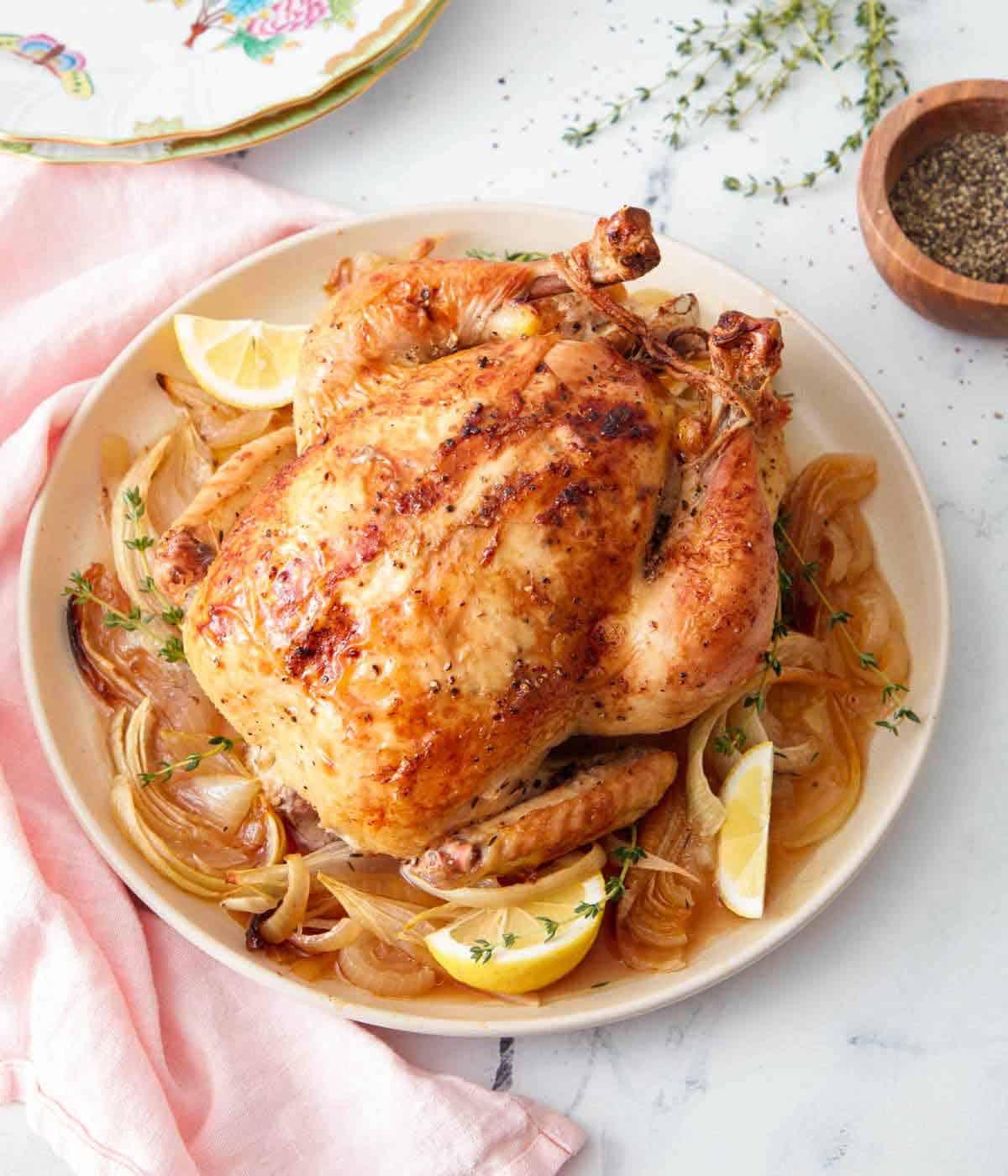A roasted chicken on a plate of cooked onions and fresh lemon wedges.