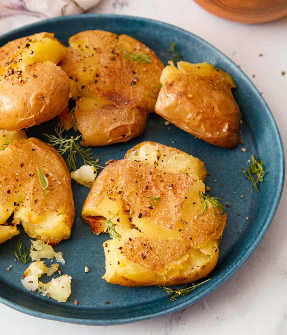 A blue plate with five pieces of smashed potatoes with freshly chopped dill on top.