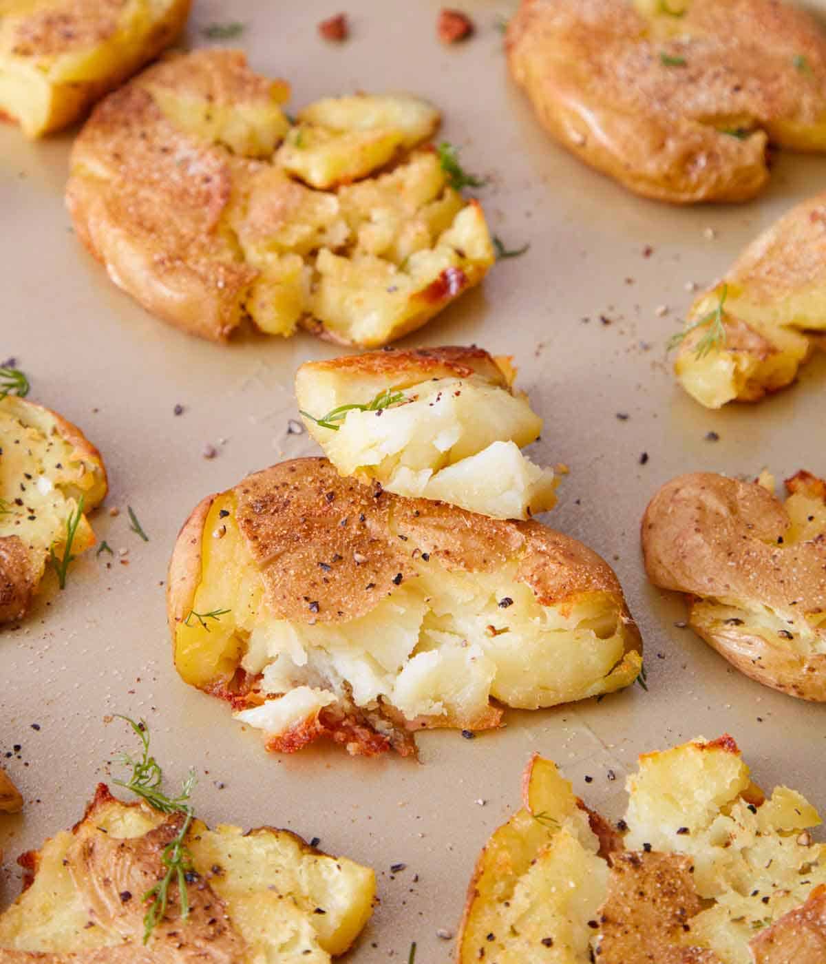 Smashed potatoes on a sheet pan with fresh dill scattered on top.