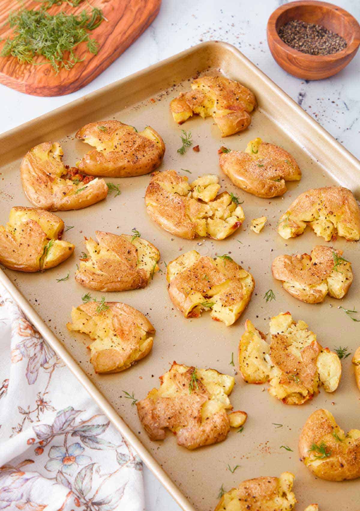 A sheet pan with multiple smashed potatoes with fresh dill and pepper on the side.