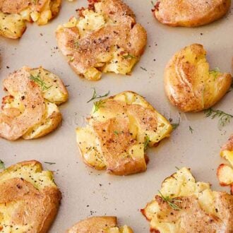 A sheet pan with smashed potatoes with freshly chopped dill and pepper on top.