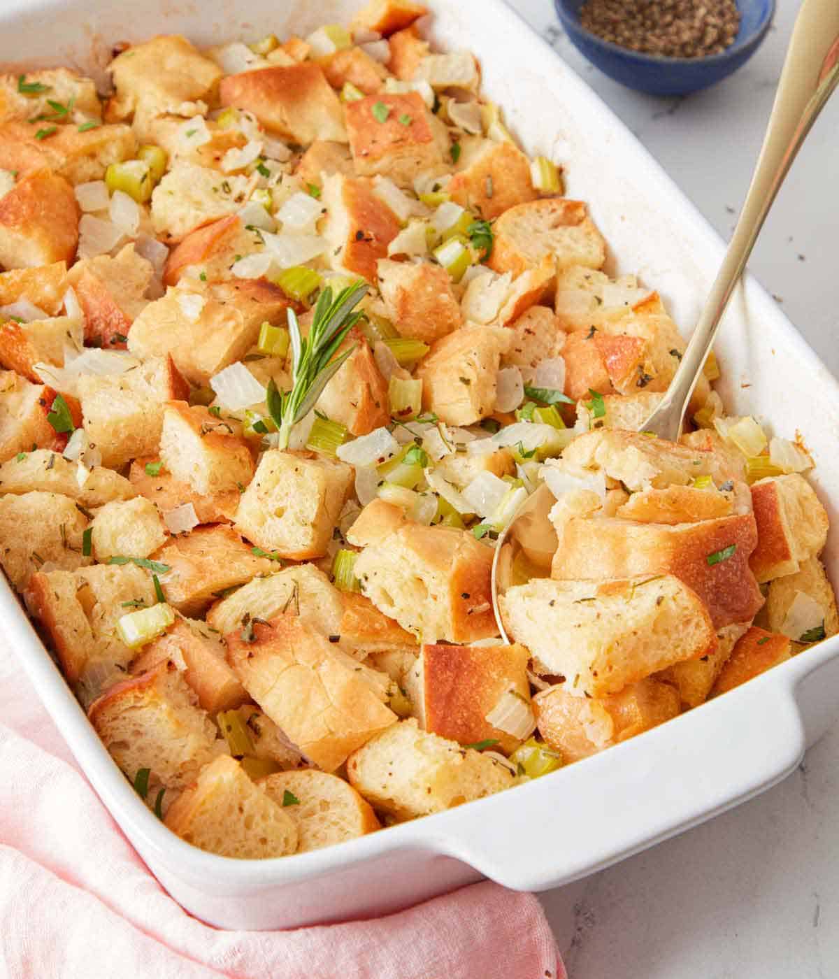 A baking dish with stuffing with a spoon tucked in.