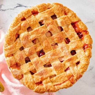 Overhead view of a whole apple cranberry pie with a pink linen and spatula on the side.