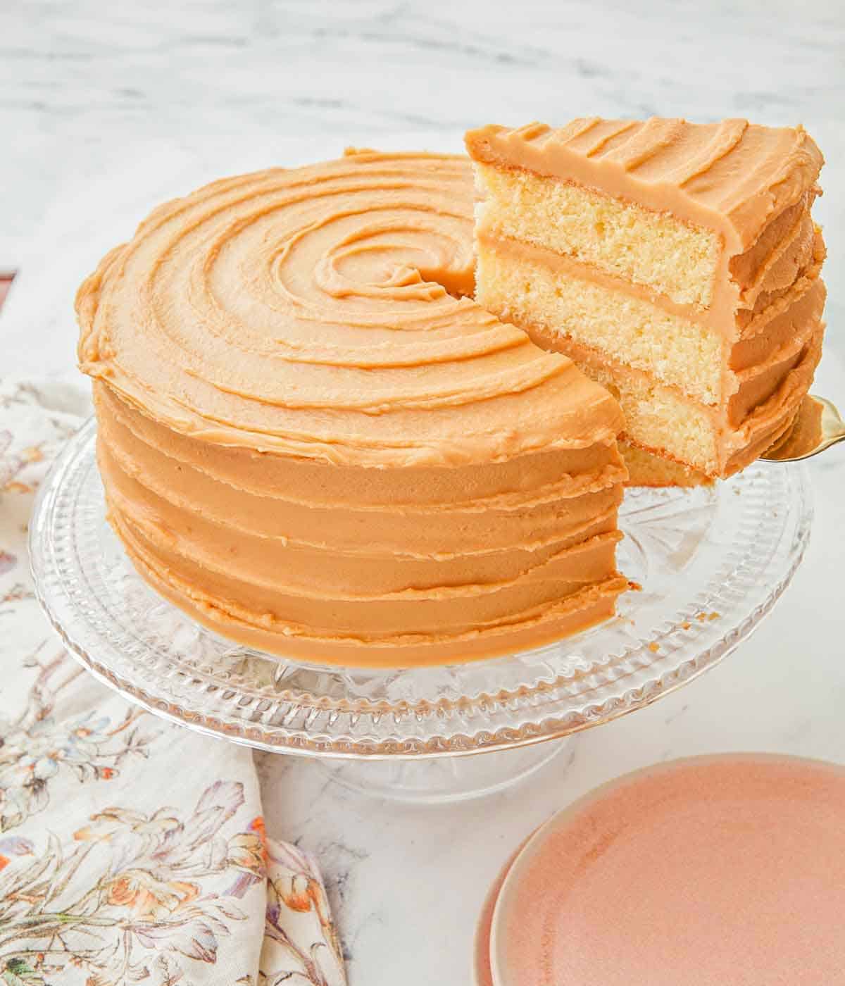 A slice of caramel cake sliced and lifted from the cake on a cake stand.