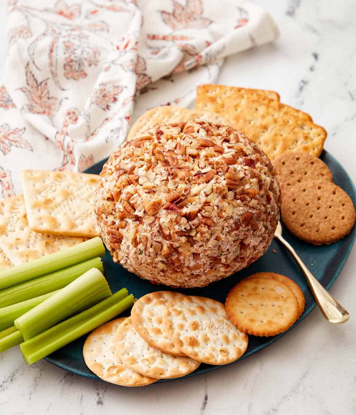 A cheese ball on a blue plate with crackers and celery surrounding it.