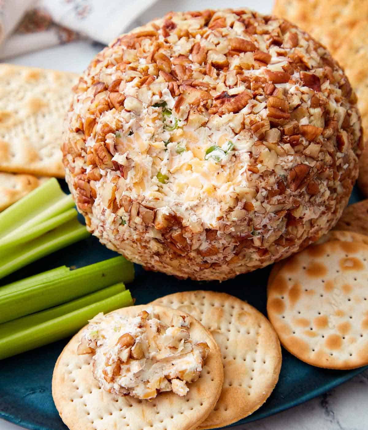 Close up of a cheese ball with a bit spread onto a cracker in front of it.