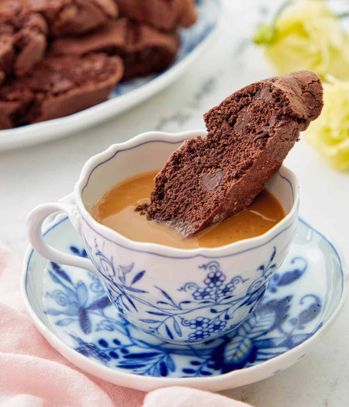 A chocolate biscotti dipped into a cup of coffee.