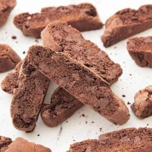 Multiple chocolate biscotti on a white surface, some stacked on each other.