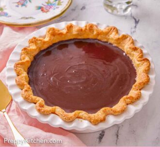 Pinterest graphic of a white baking dish with a chocolate pie with flowers and plates in the background.