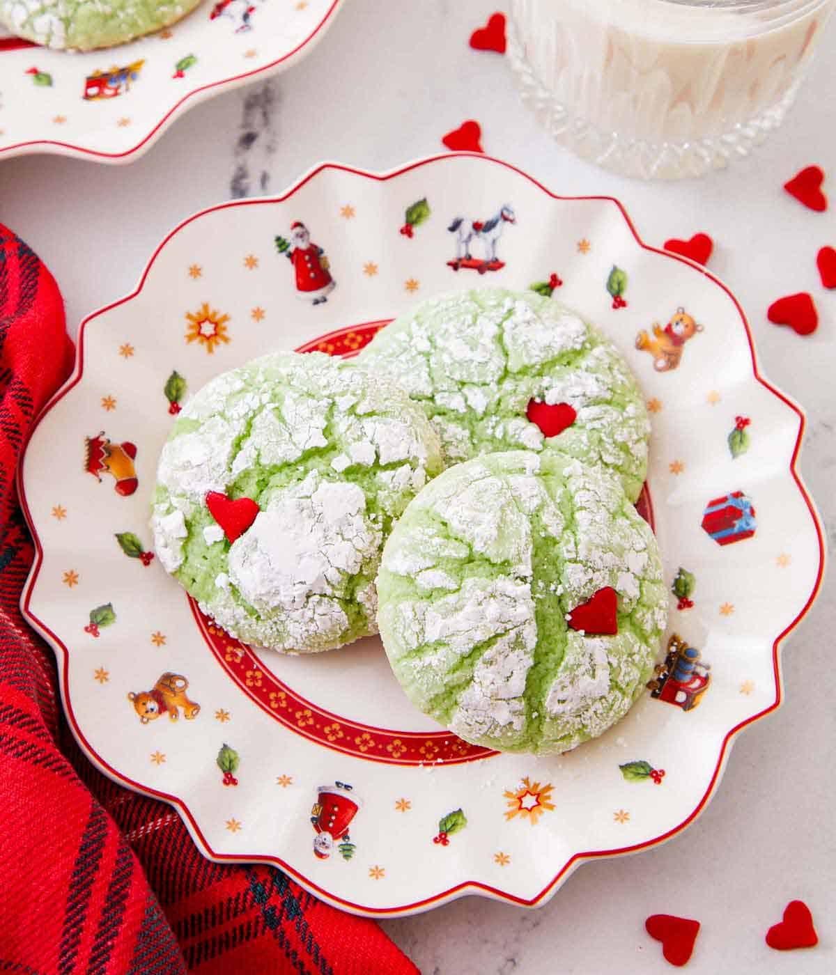 A festive plate with three Grinch cookies with heart sprinkles scattered around.