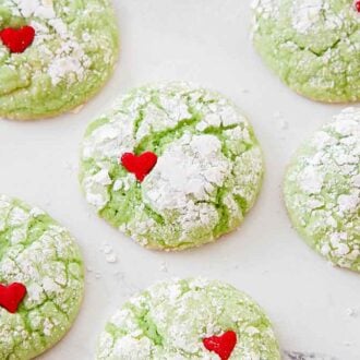 Multiple Grinch cookies with a heart sprinkle on each.