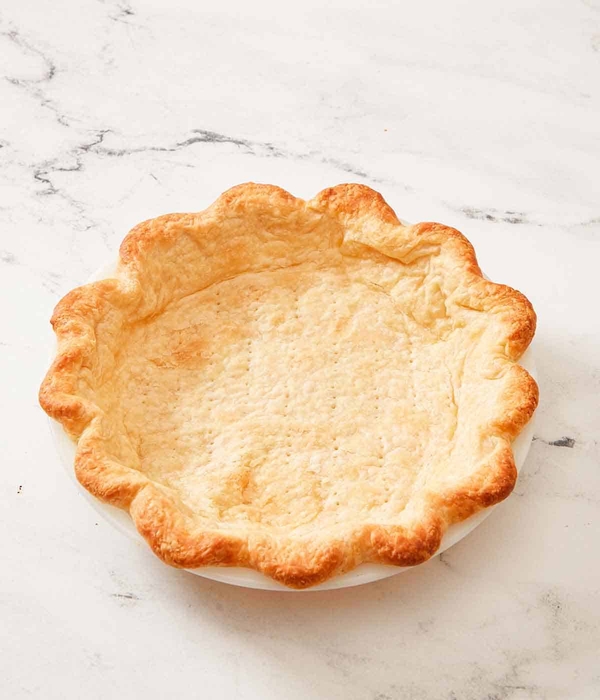 A marble surface with a baking dish with a blind baked pie crust.