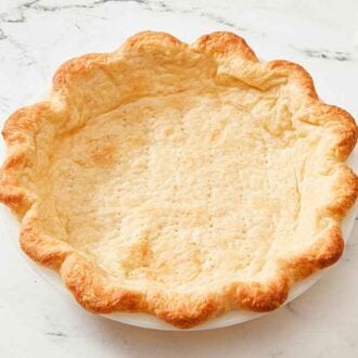 A blind baked pie crust with a parchment filled with dried beans in the background.