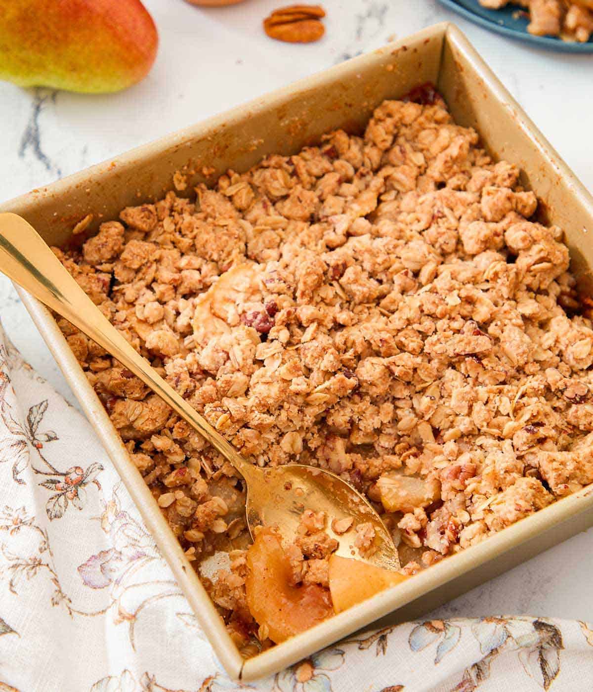 A square baking pan with pear crisp and a spoon tucked into it.