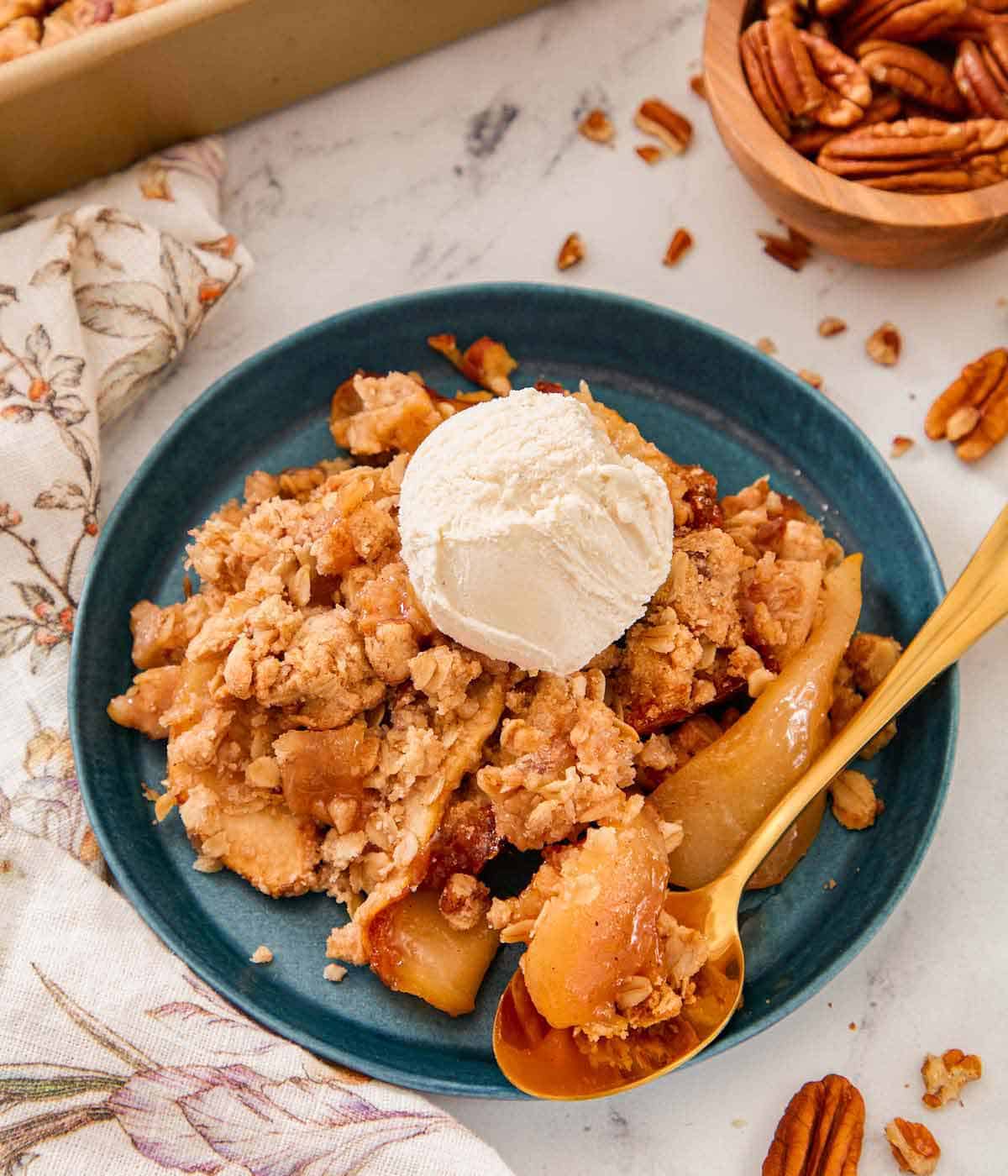A blue plate with a serving of pear crisp with a scoop of ice cream on top and a spoon by it.