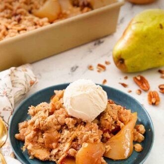 Pinterest graphic of of a plate of pear crisp with a scoop of ice cream on top with a fresh pear in the background along with the baking dish.