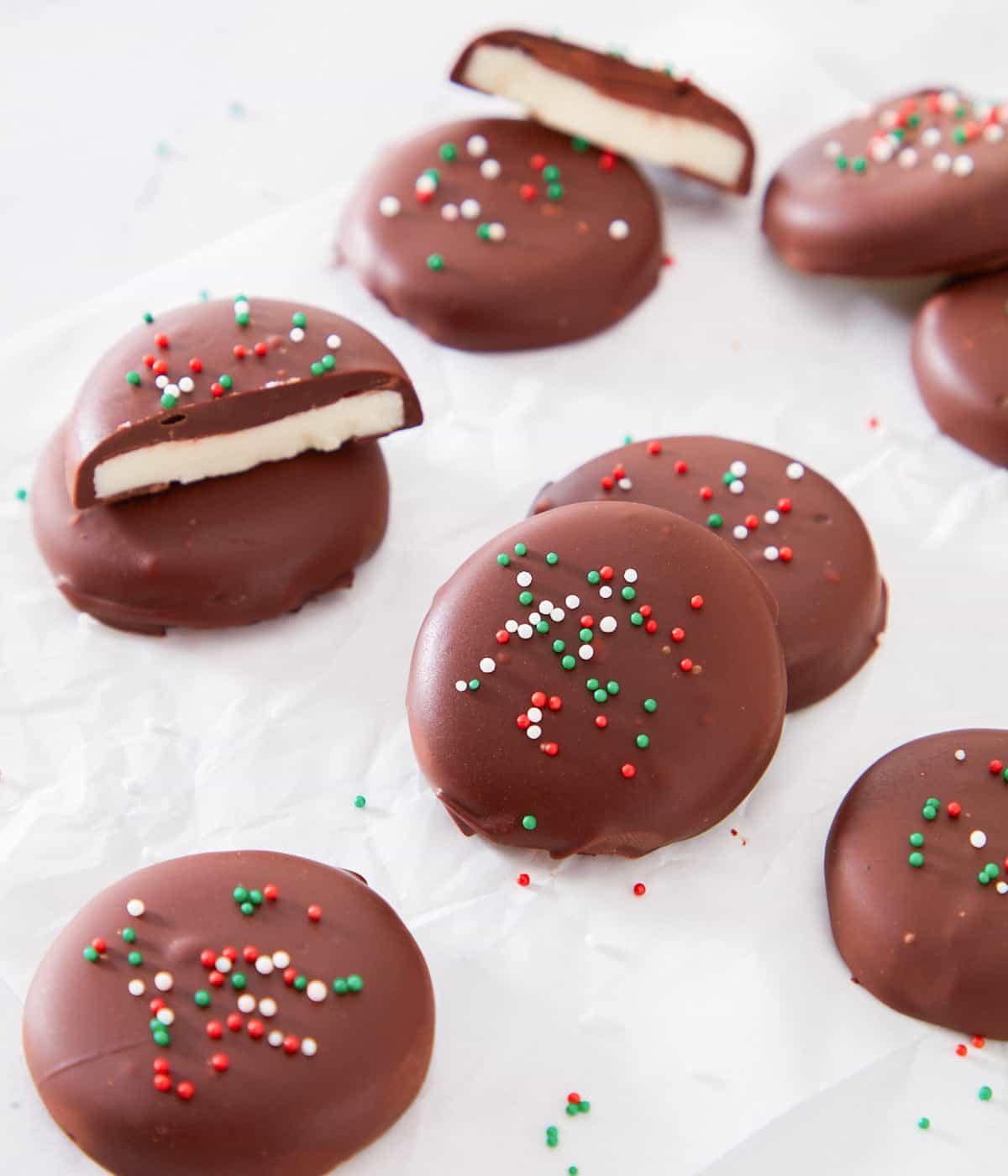Multiple pieces of peppermint patties on a white surface with red, white, and green sprinkles on top. Some pieces are cut in half.