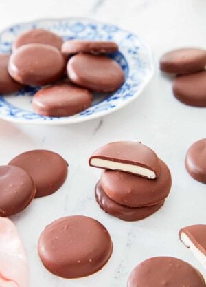 Multiple peppermint patties scattered with the focus on a stack of three in the middle, the top one cut in half.