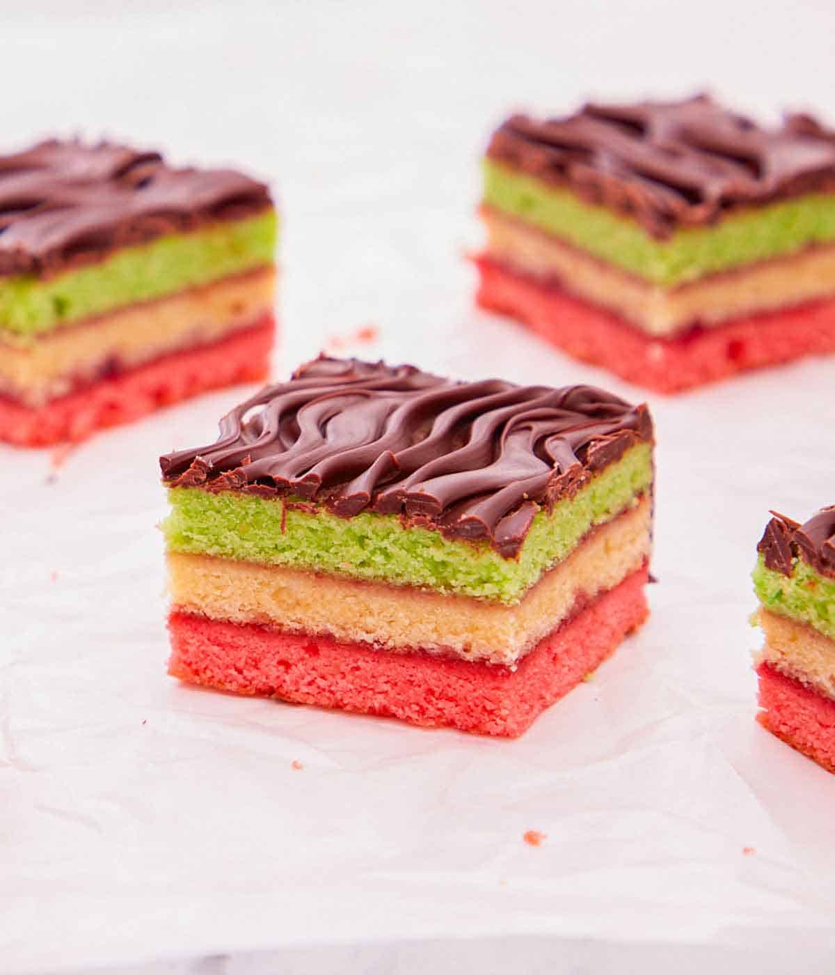 A couple of rainbow cookies with one in focus and in the middle, showing the colorful layers.
