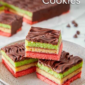 Pinterest graphic of a plate with three rainbow cookies stacked with the rest of the dessert in the background.