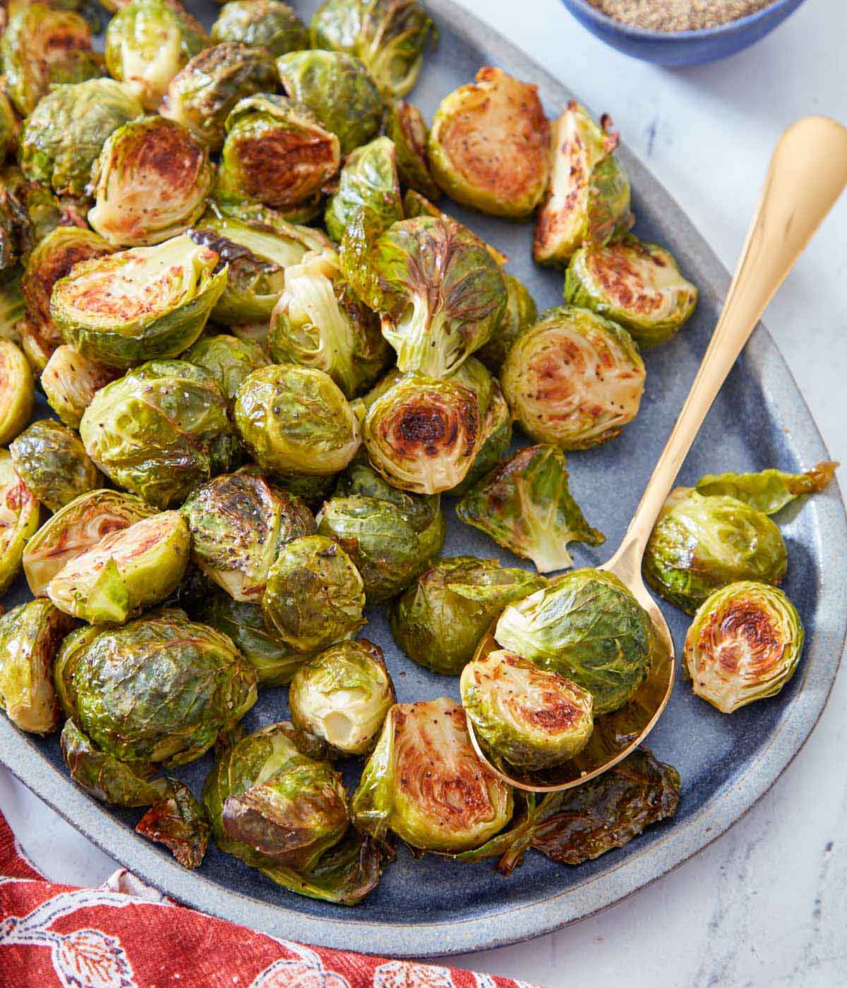 An oval serving platter of roasted Brussels sprouts with a golden spoon holding two sprouts.