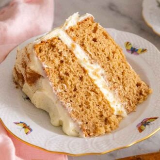 A slice of spice cake with cream cheese frosting between the two cake layers. Cinnamon sticks on the side.