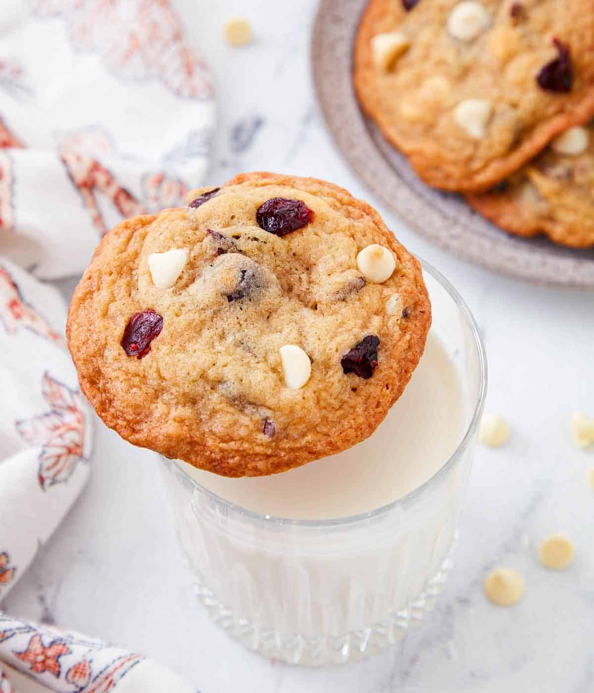 Overhead view of a white chocolate cranberry cookie on top of a glass of milk.