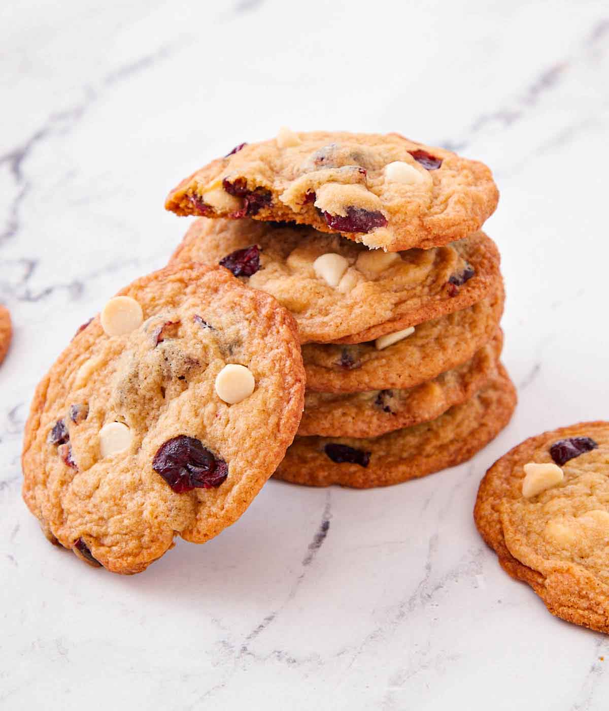 A stack of white chocolate cranberry cookies with one leaning on the stack.