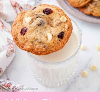 Pinterest graphic of a glass of milk with a white chocolate cranberry cookie placed on its rim.